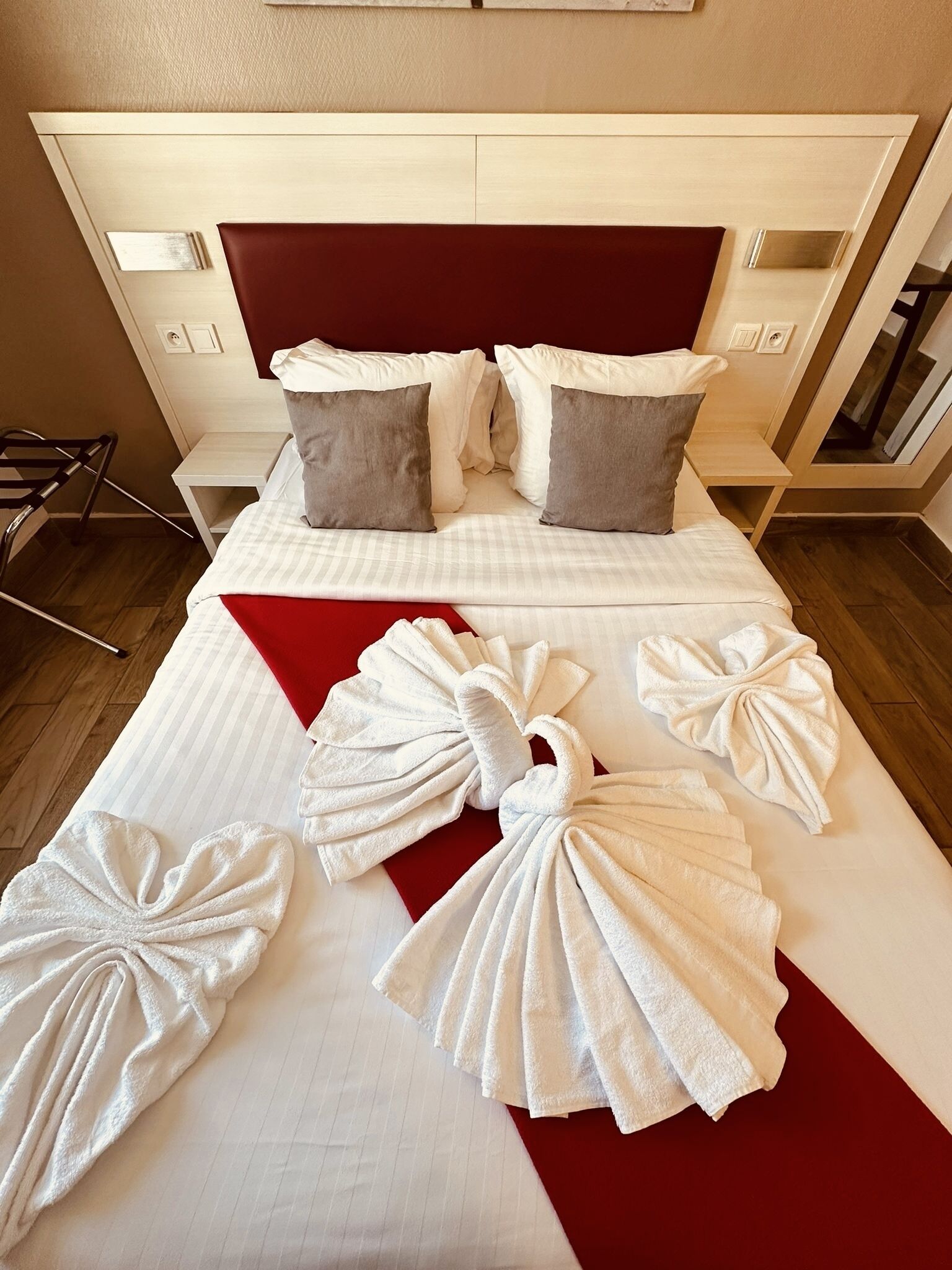 A hotel room with a bed, pillows, a red throw, and towels arranged on the bed.