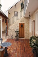 Una terraza de madera con barandilla de metal, una puerta y un muro de piedra, además de una escalera.