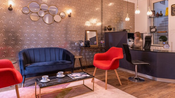 A modern living room with a blue sofa, a red chair, a coffee table with a magazine, and a mirror wall. - Hôtel Istria by Magna Arbor (Paris)