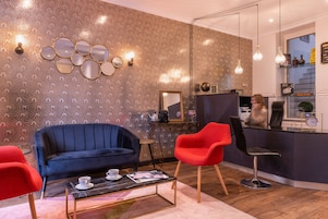 Una sala de estar moderna con un sofá azul, un sillón rojo, una mesa de centro con una revista y una pared de espejo.