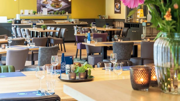 Interior de un restaurante con mesas dispuestas para comer, sillas y un jarrón grande con flores.