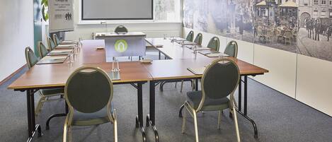 A conference room with a long table, chairs, a projector screen, and a large poster on the wall.