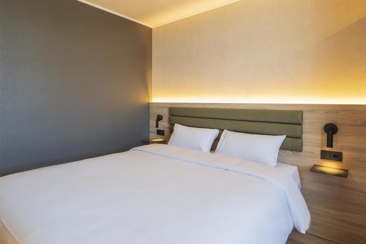 Cama bem arrumada com lençóis brancos num quarto de hotel moderno.