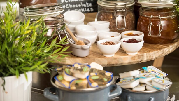 Diversos productos alimenticios, incluyendo tarros de miel, chocolate y conservas de frutas, junto con recipientes pequeños con especias y semillas.