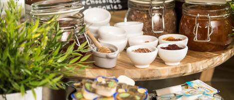 Diversos productos alimenticios, incluyendo tarros de miel, chocolate y conservas de frutas, junto con recipientes pequeños con especias y semillas.
