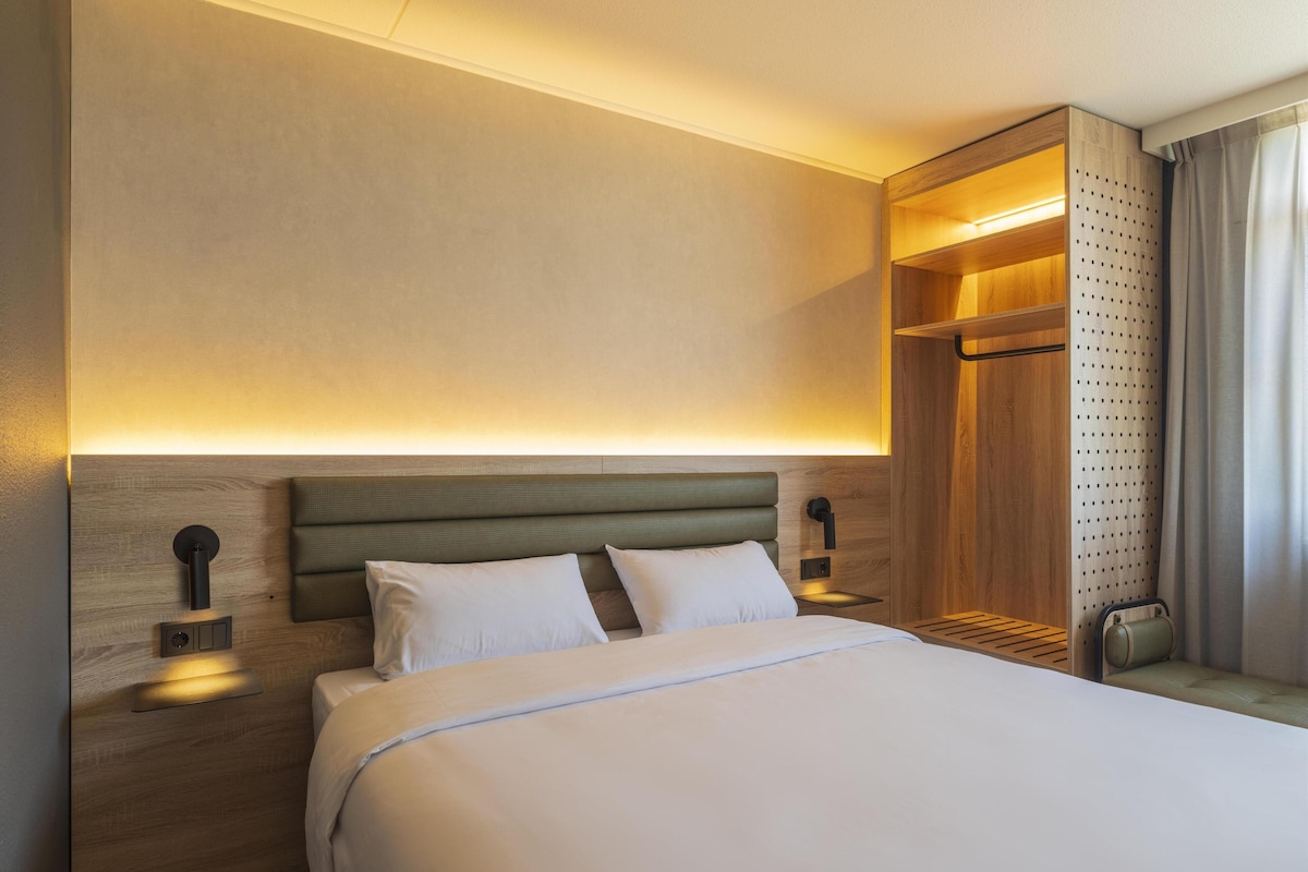 A hotel room with a large bed, wooden headboard, bedside tables, and a built-in wardrobe.