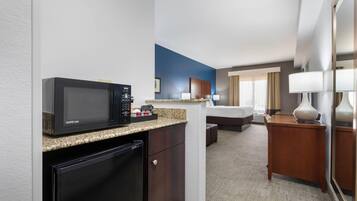 A compact hotel room with a kitchenette, a bed, a desk, and a mirror.