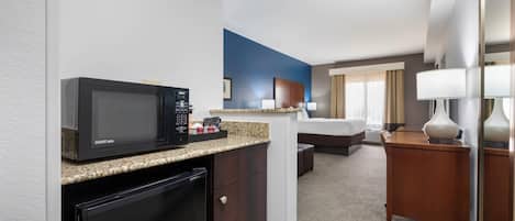 A compact hotel room with a kitchenette, a bed, a desk, and a mirror.