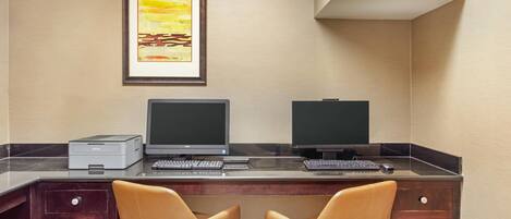 Una oficina de hotel con dos escritorios, computadoras, una impresora y dos sillones de cuero.