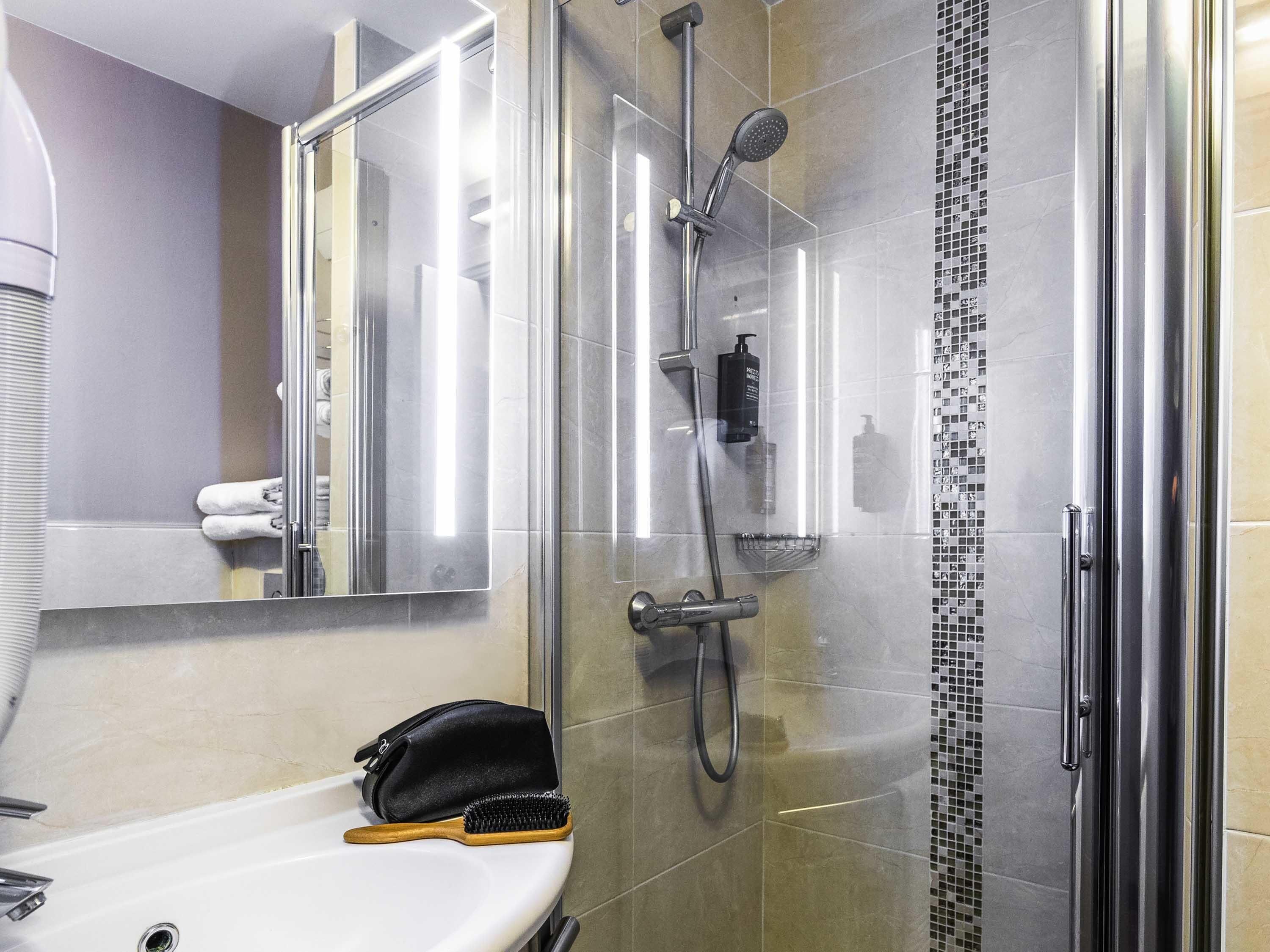 Un baño moderno con cabina de ducha de vidrio, un lavamanos con toallero y un espejo.