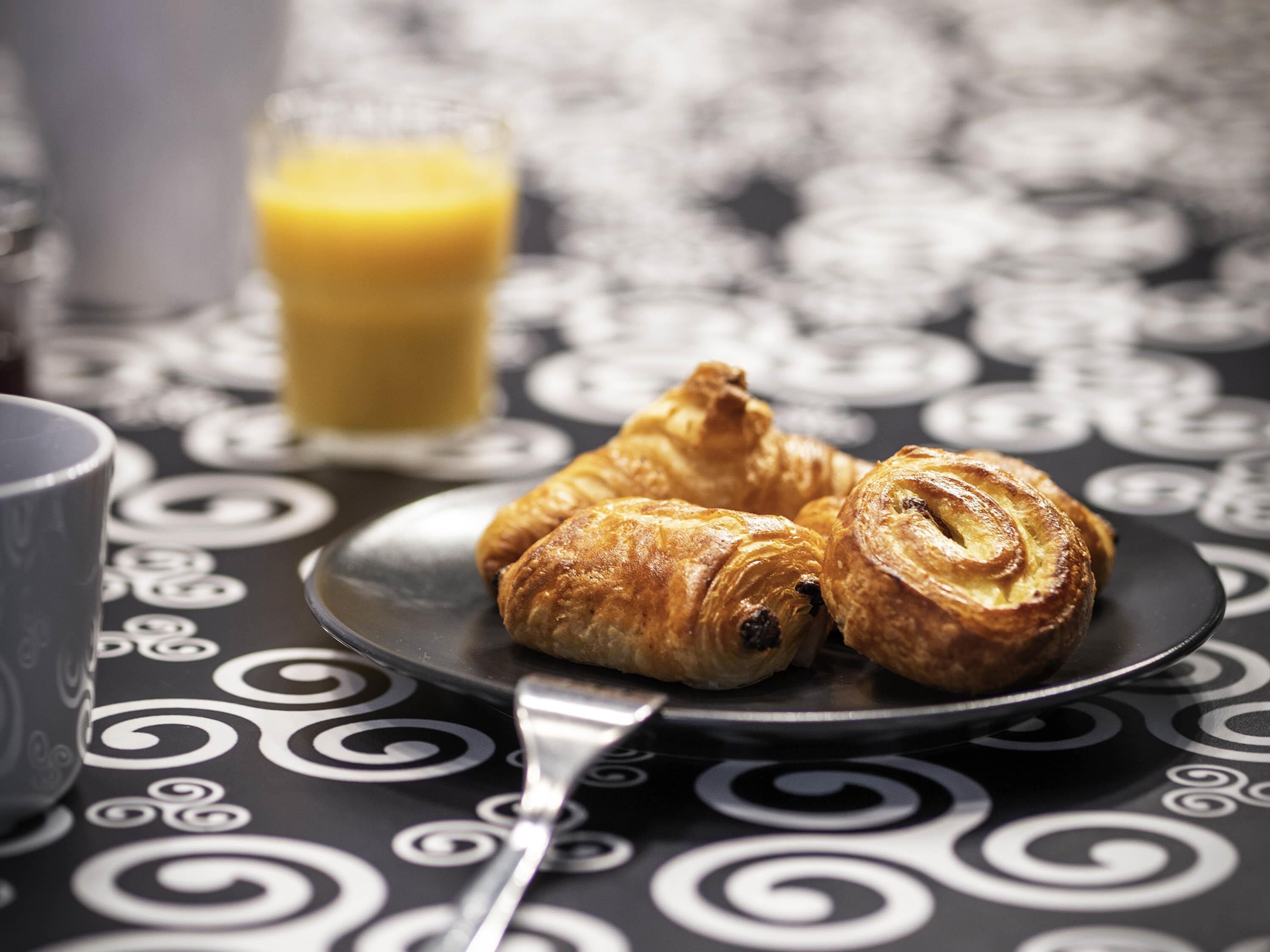 A plate with croissants and a glass of orange juice on a table with a black and white pattern.