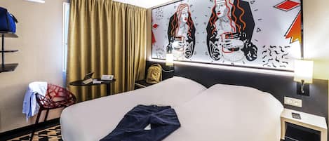 Habitación de hotel con cama, escritorio, silla, lámpara y un cuadro en la pared.