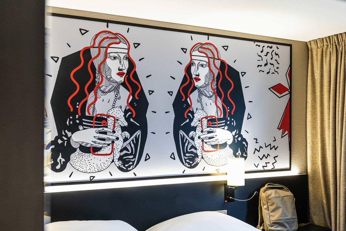 Una habitación de hotel con una cama, una mesita de noche y una obra de arte colgada en la pared.