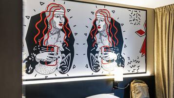 Una habitación de hotel con una cama, una mesita de noche y una obra de arte colgada en la pared.