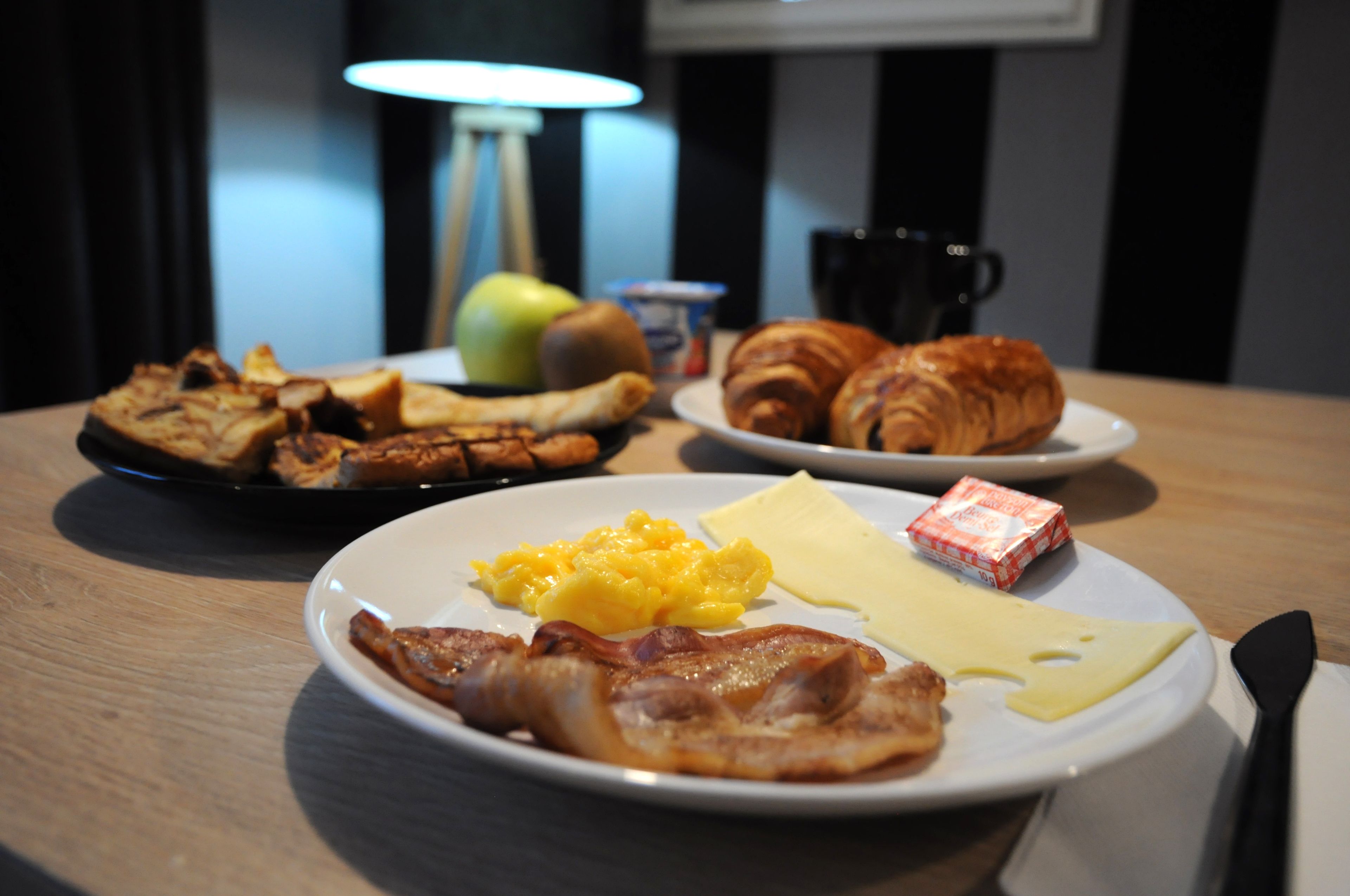 A breakfast table with plates of eggs, bacon, cheese, croissants, and toast.