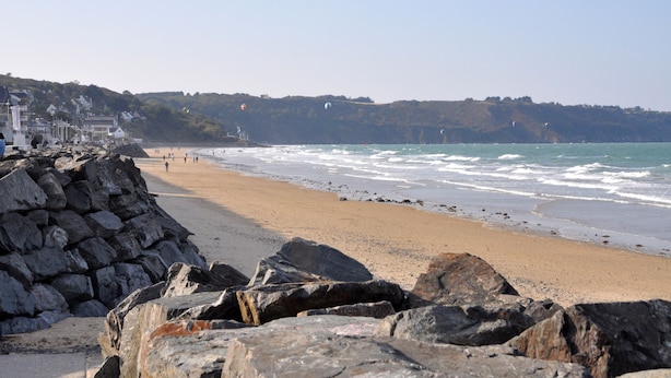 A beach with rocky foreground, a sandy shore, and a cliff with buildings in the background. - Ibis Styles Saint Brieuc Plerin (Plerin)