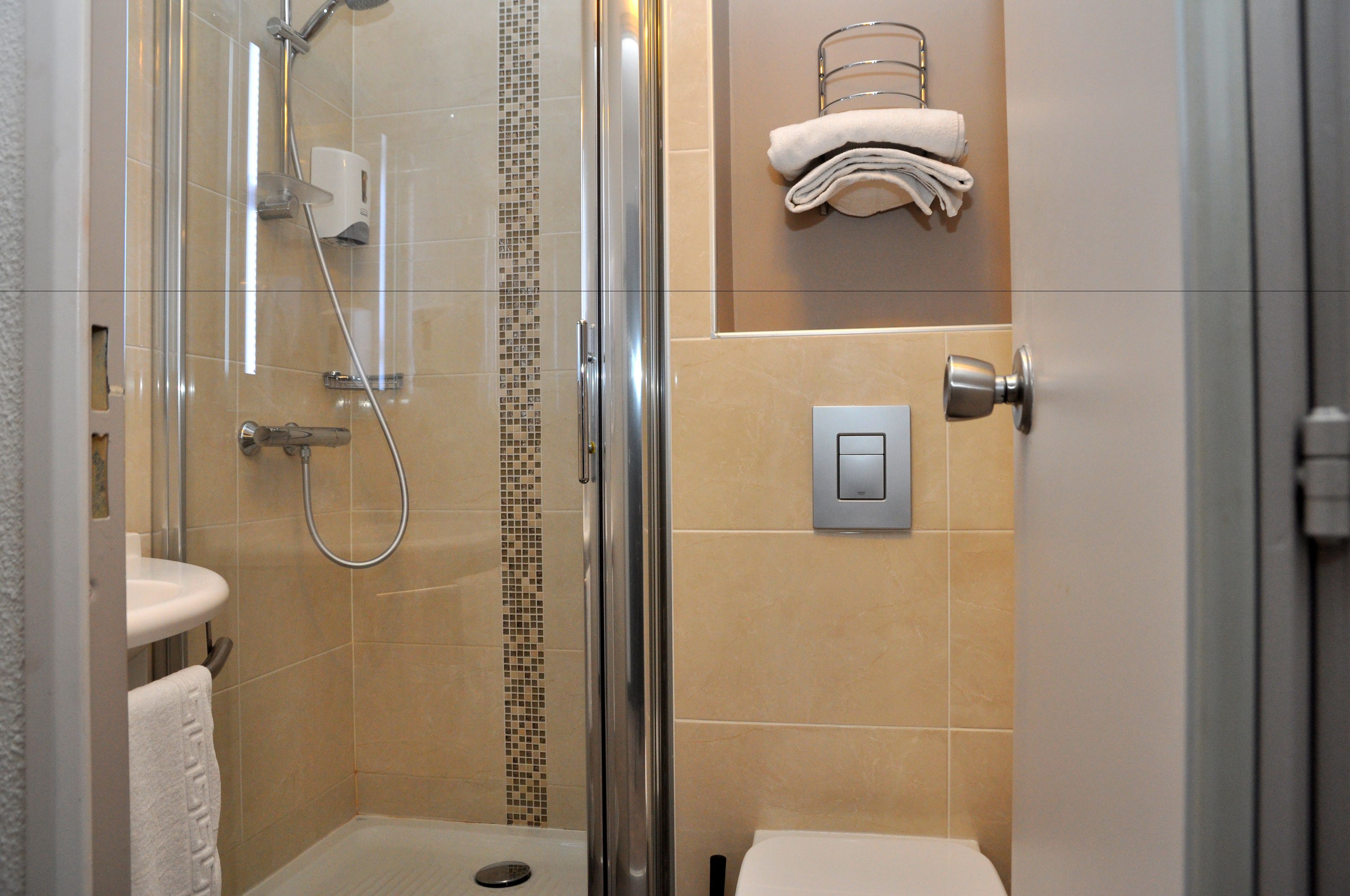 A modern bathroom with a glass shower enclosure, a white sink, and a towel rack with folded towels.