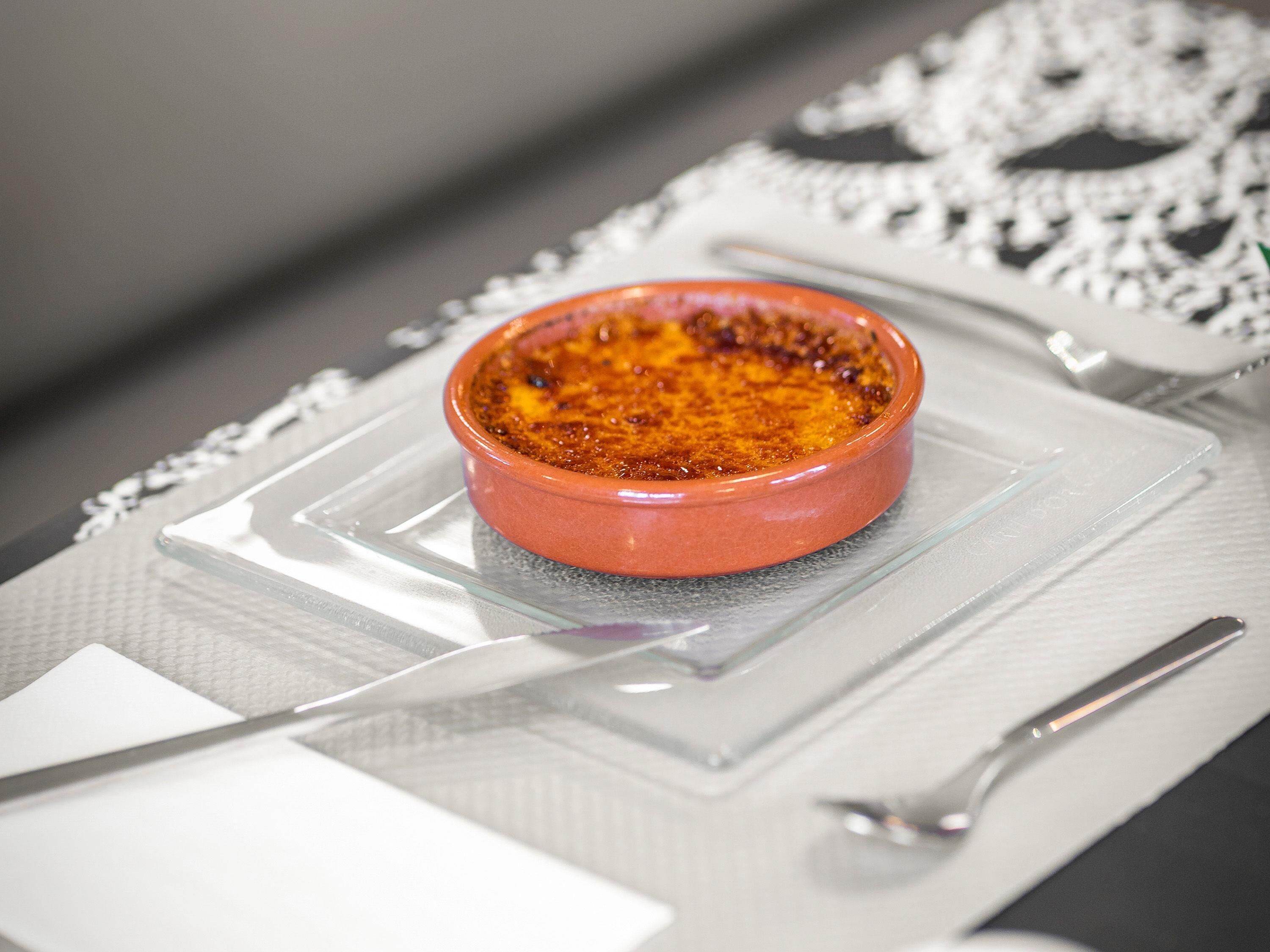 A dessert in a ceramic dish on a clear glass plate, with a silver spoon beside it.
