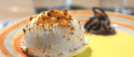 A dessert on a plate with a yellow base and a white mound topped with brown crumbs.
