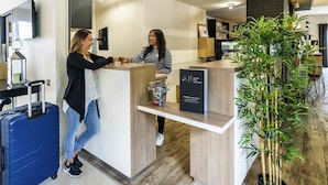 A reception desk with a sign reading "Priority Welcome" and a blue suitcase on the floor. - Ibis Styles Saint Brieuc Plerin (Plerin)