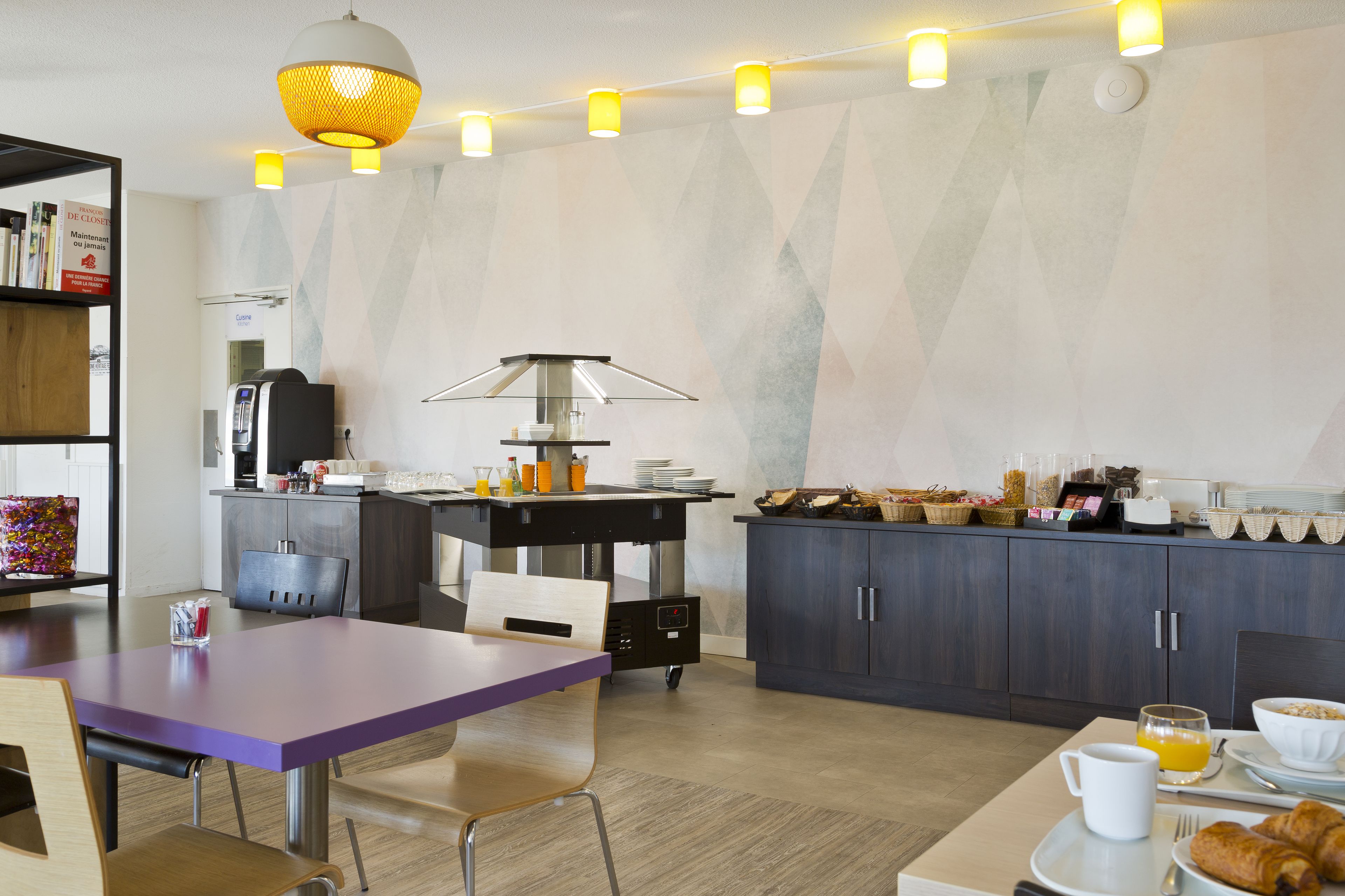 Een moderne keuken met een eethoek, voorzien van een koffieapparaat, ontbijtartikelen en een bijzondere hanglamp.
