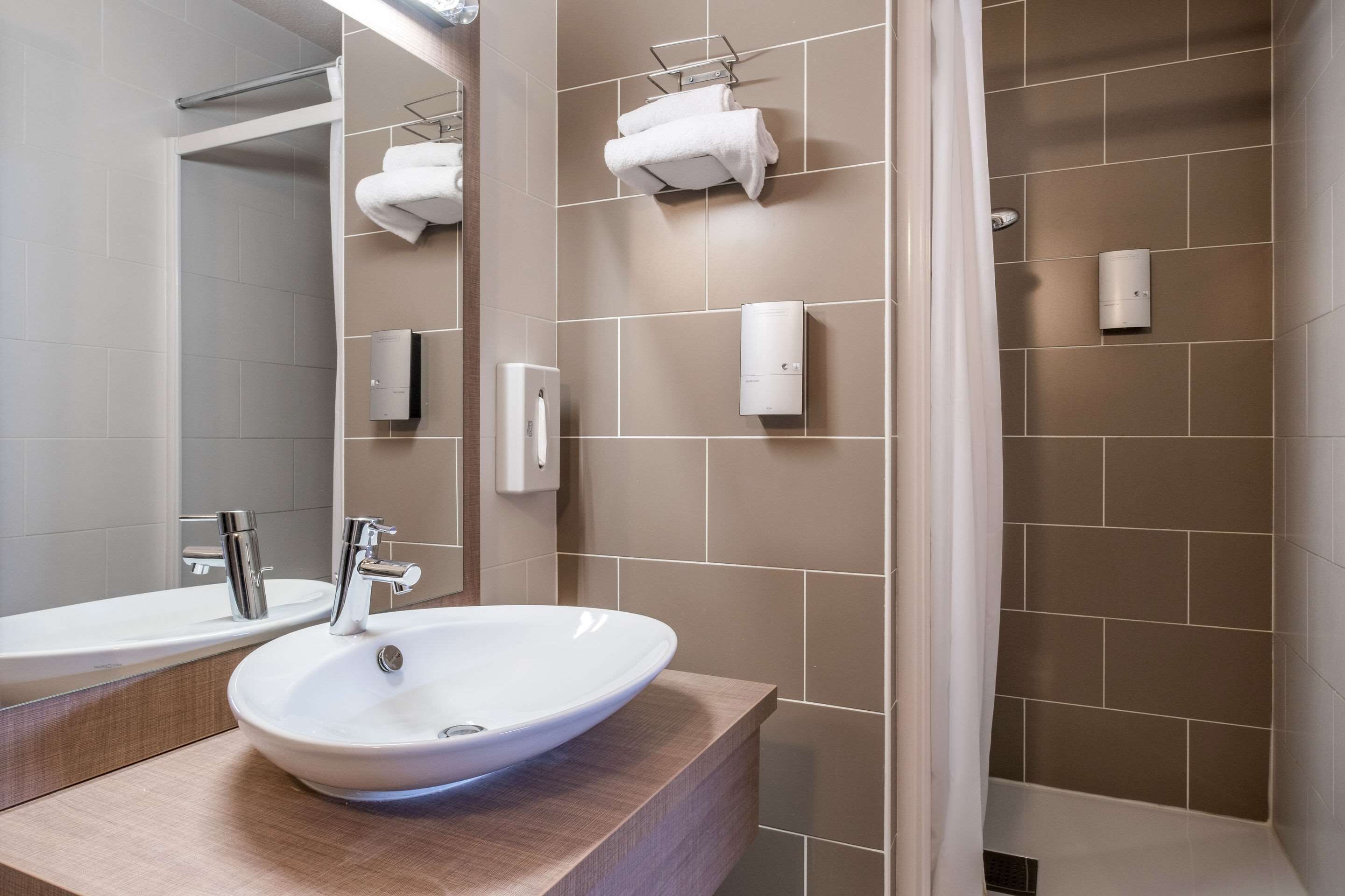 Un baño moderno con un espejo grande, dos lavamanos, zona de ducha y toalleros.