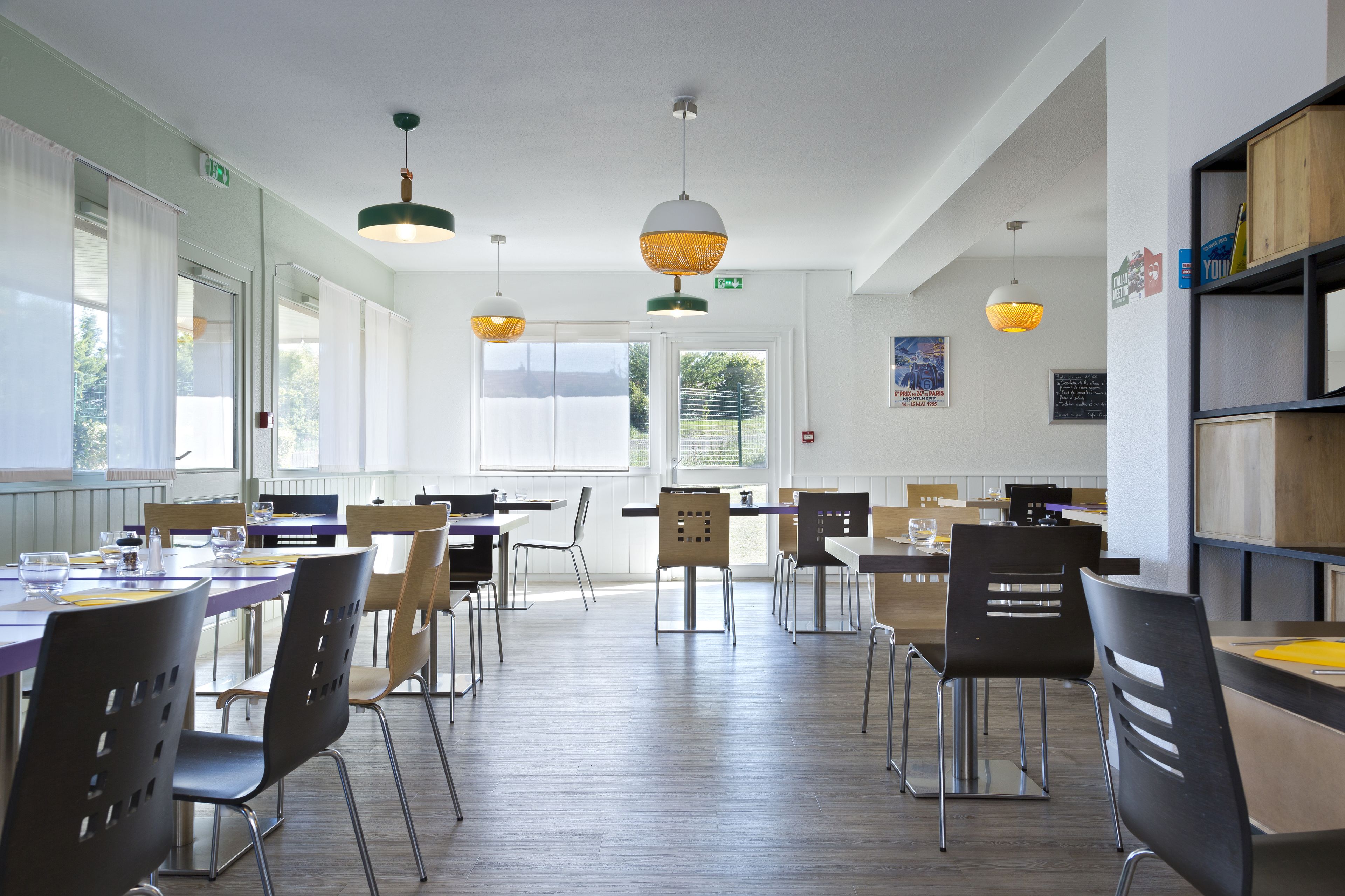 Un comedor con varias mesas y sillas, iluminación colgante y vistas al exterior.