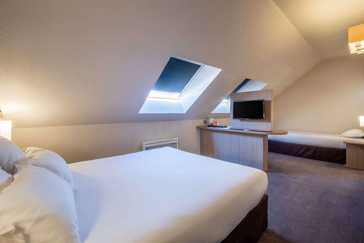 Habitación de hotel con dos camas, un escritorio, un televisor de pantalla plana y tragaluces.