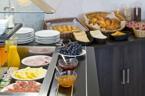 A breakfast buffet with various food items including bread, pastries, cheese, and fruits.