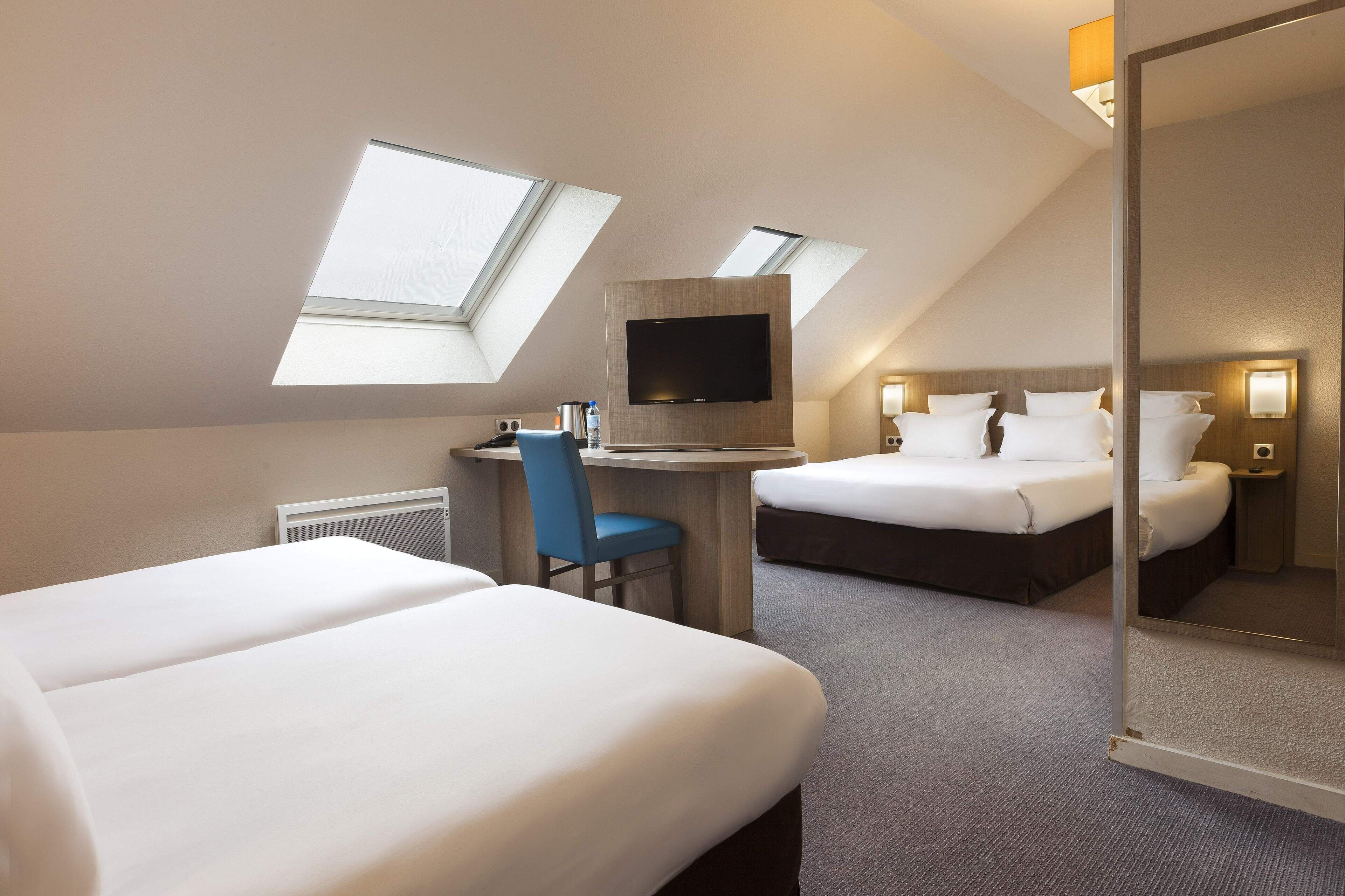 Une chambre d’hôtel avec deux lits, un bureau, une chaise, une télévision et des fenêtres de toit.