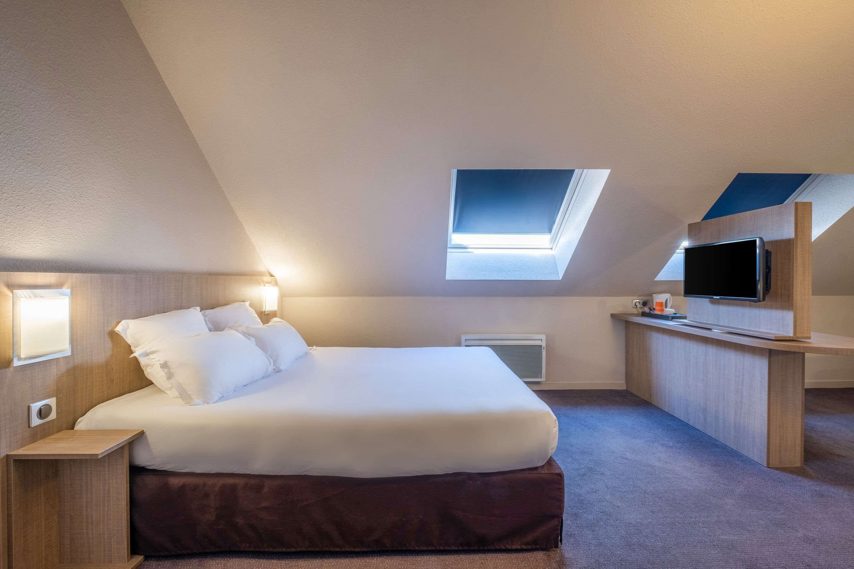 A modern bedroom with a skylight, a bed, a desk, and a flat-screen TV.