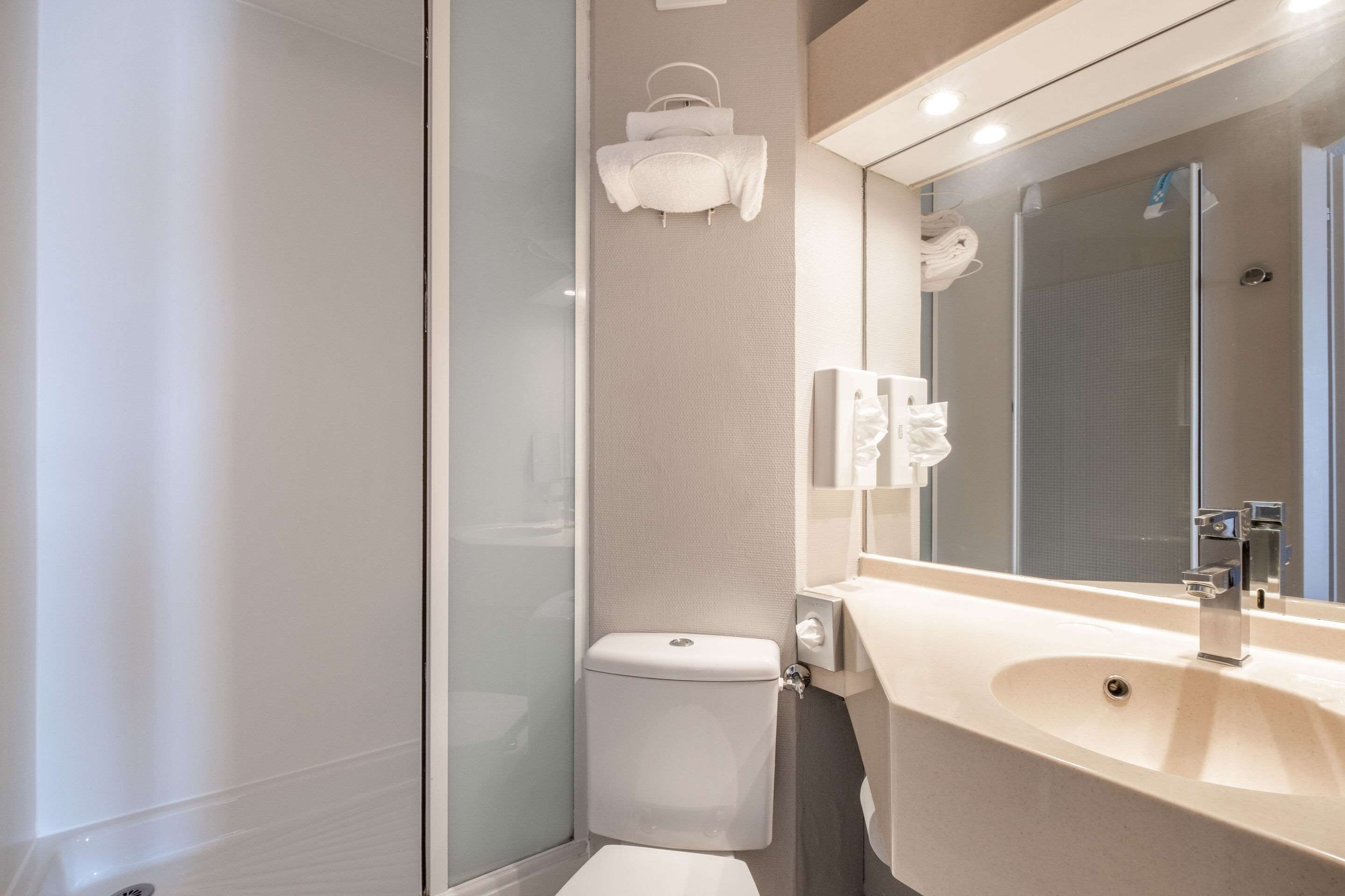 A modern bathroom with a glass shower enclosure, a toilet, a sink with a mirror, and towel hooks on the wall.