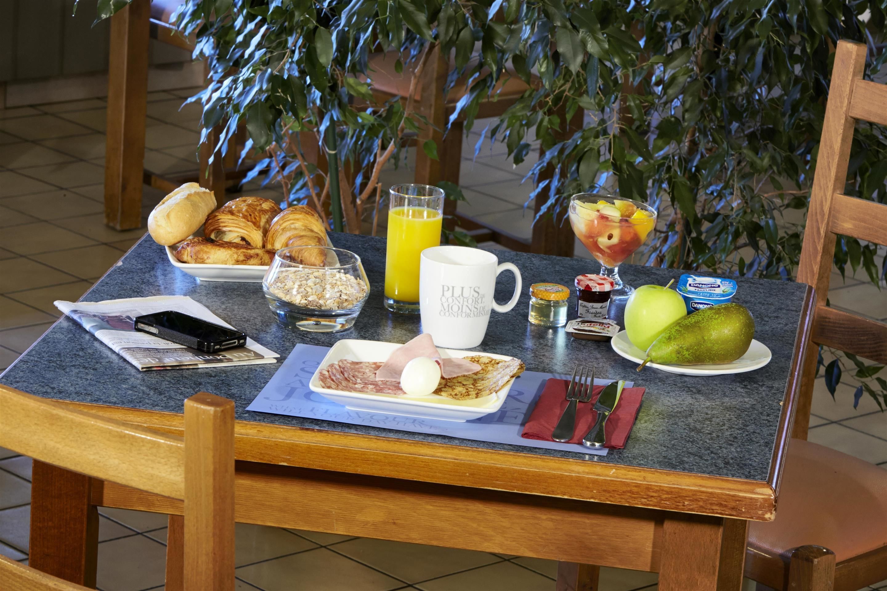 A breakfast table with croissants, a glass of orange juice, a fruit salad, a plate with a pear, and a cup labeled "Plus."