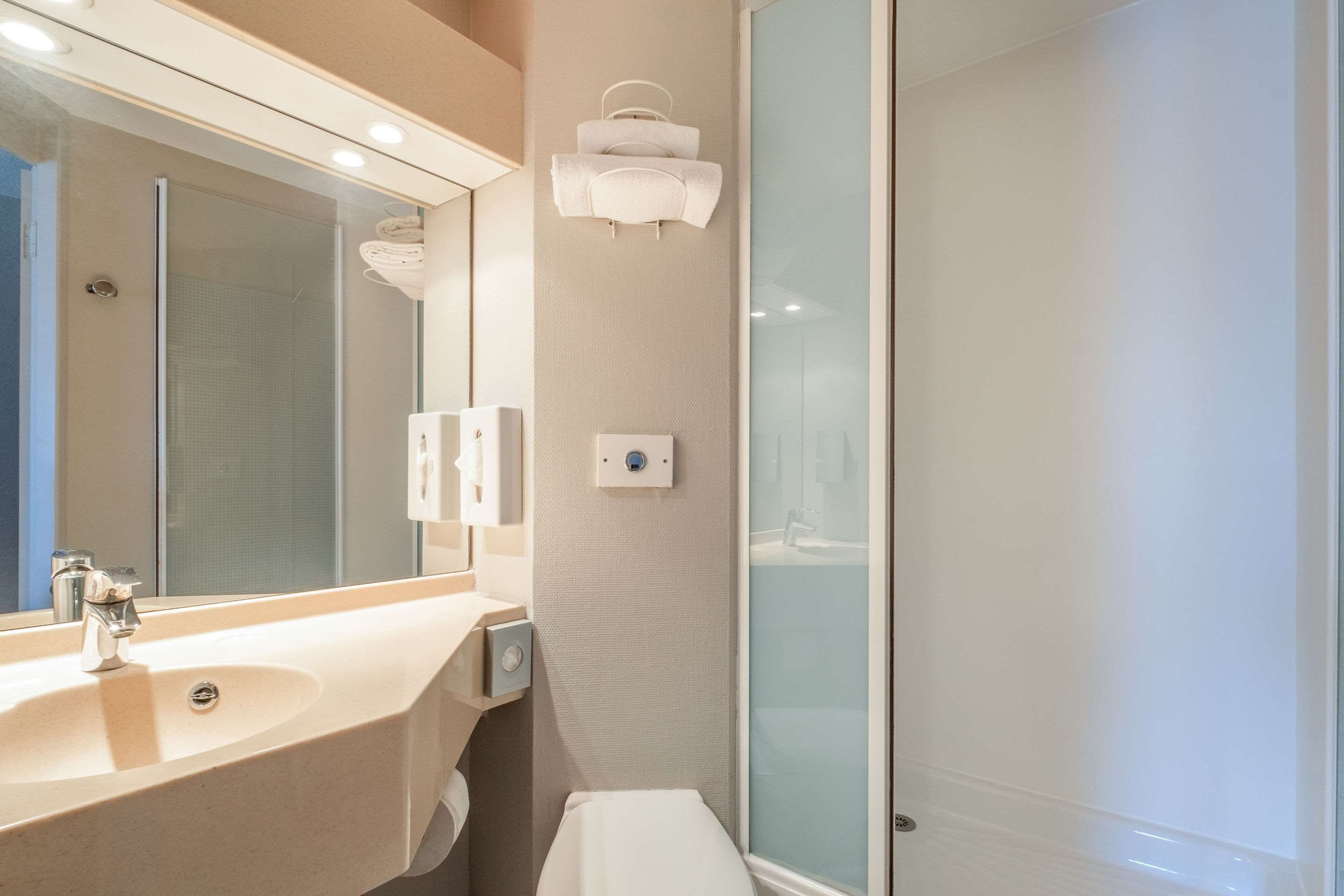 Un baño moderno con lavamanos, espejo, toallero y cabina de ducha de vidrio.