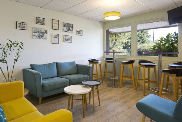 A room with a sofa, chairs, a small table, and bar stools. There are framed pictures on the wall and a window with a view of trees.