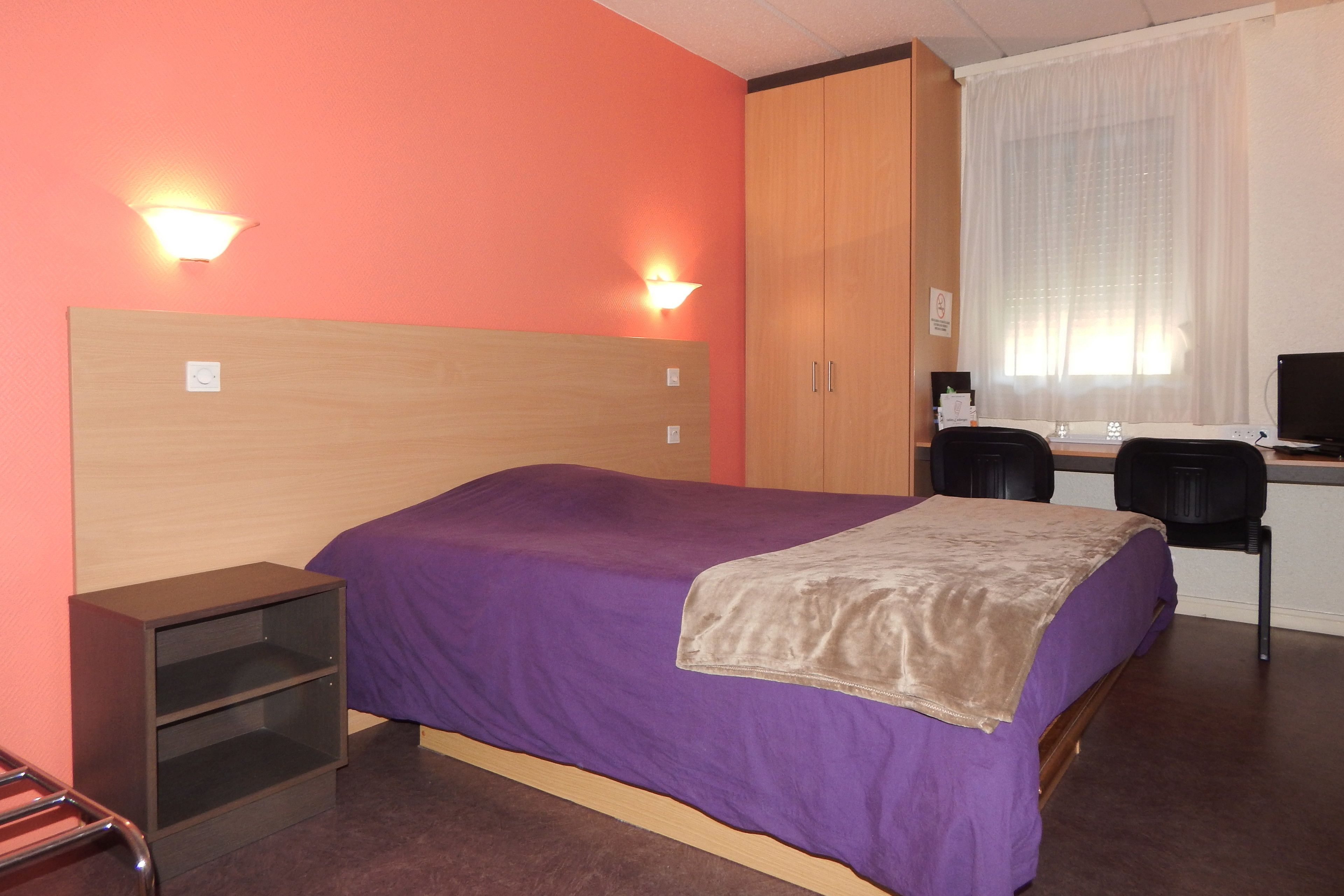 A hotel room with a bed, a desk, and a chair.