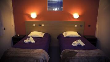 Een hotelkamer met twee bedden, elk met een paarse sprei en witte kussens, en een houten hoofdbord. Er staan twee nachtkastjes met lampen, en er hangt een lijst met een afbeelding aan de muur boven de bedden.