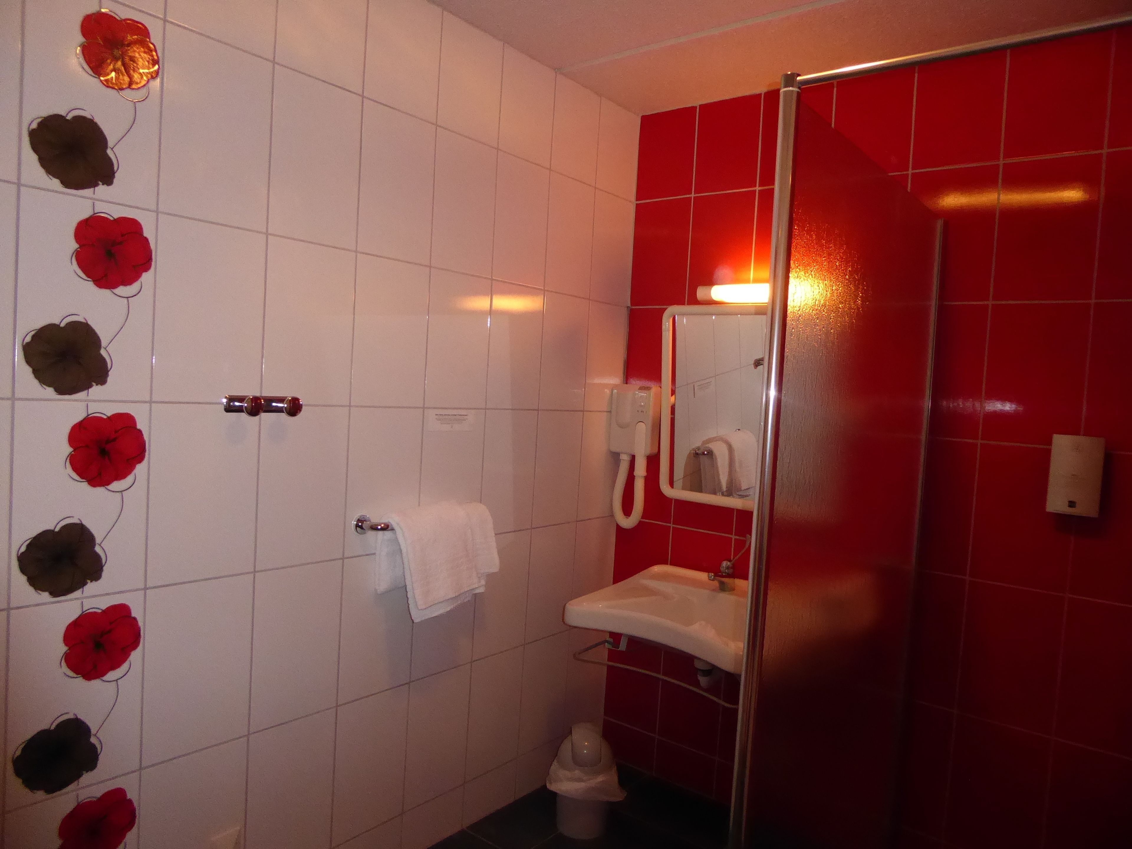 A bathroom with red tiles, a white sink, a mirror, a towel rack, and decorative wall flowers.