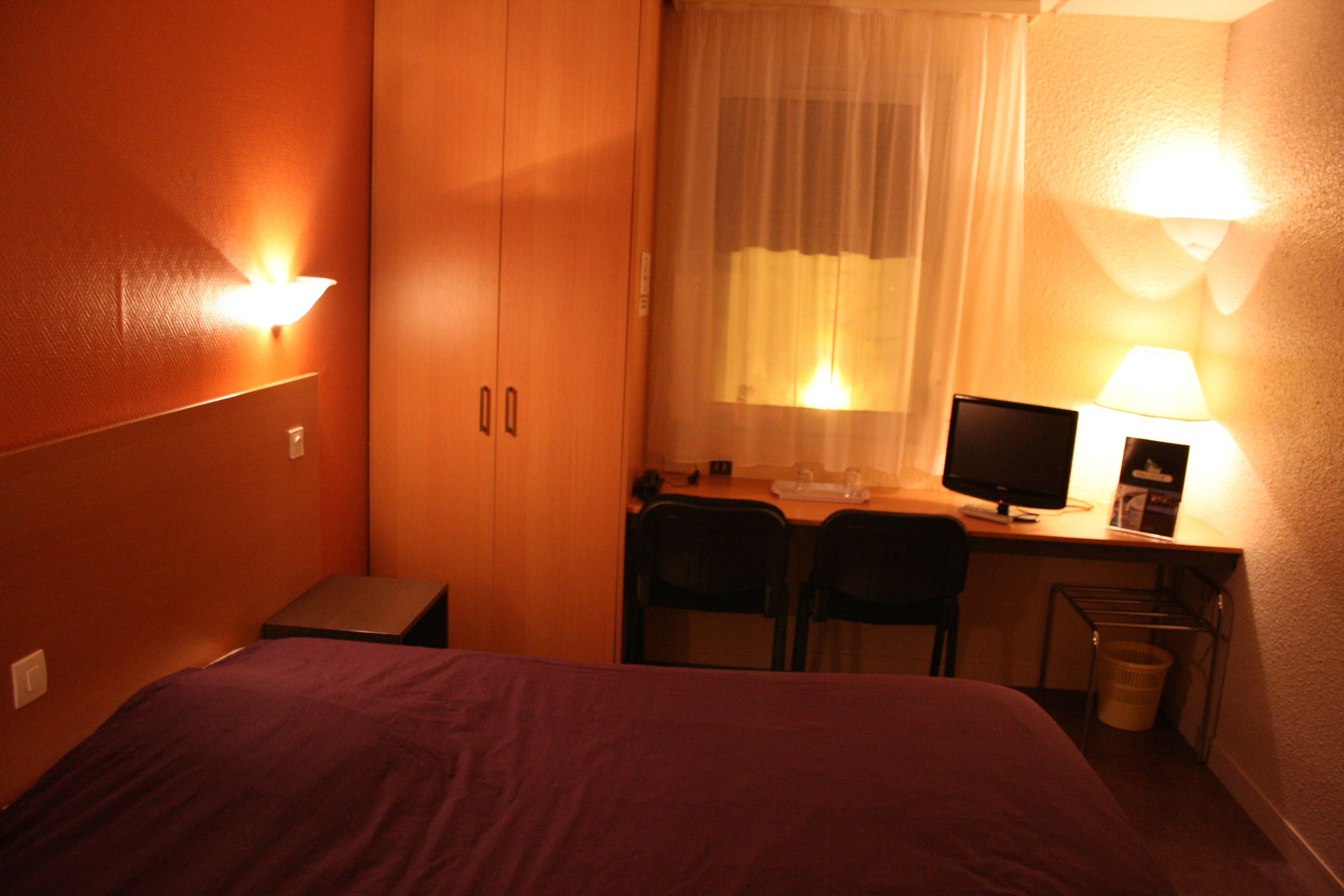 A hotel room with a bed, a desk with a computer, two chairs, a small table, and a waste basket.