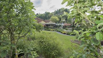 A garden with a gazebo, a pond, and a building with a red roof.