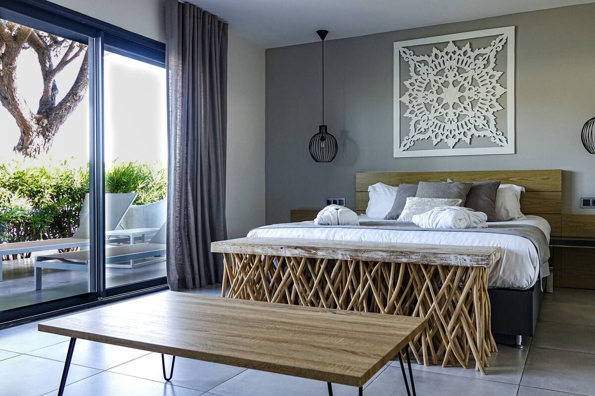 A modern bedroom with a large bed, a wooden bench, two bedside tables, and a decorative wall piece.