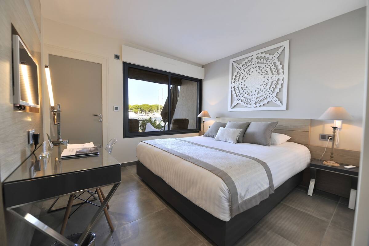 A modern bedroom with a large bed, a glass desk, and a view of the outdoors.