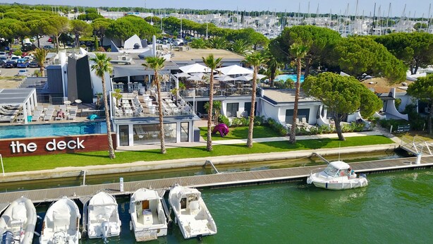 A marina with boats docked, a swimming pool, and a deck area with lounge chairs and umbrellas. - Le Spinaker Boutique Hôtel Restaurant (Le Grau-Du-Roi)