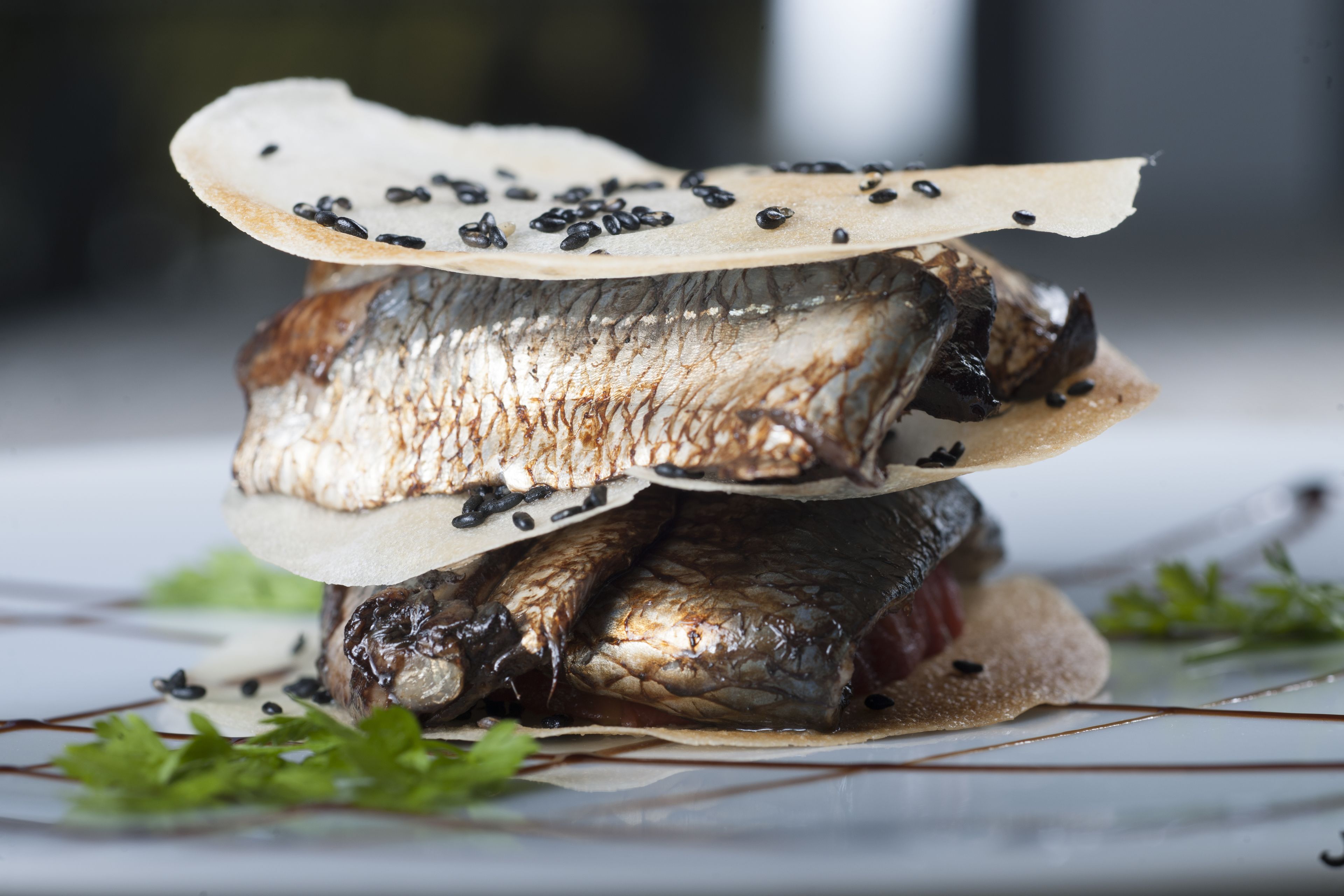 A stack of grilled fish with a piece of bread on top, garnished with black sesame seeds.