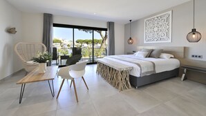 A modern bedroom with a large bed, a dining table, and a view of the city. - Le Spinaker Boutique Hôtel Restaurant (Le Grau-Du-Roi)