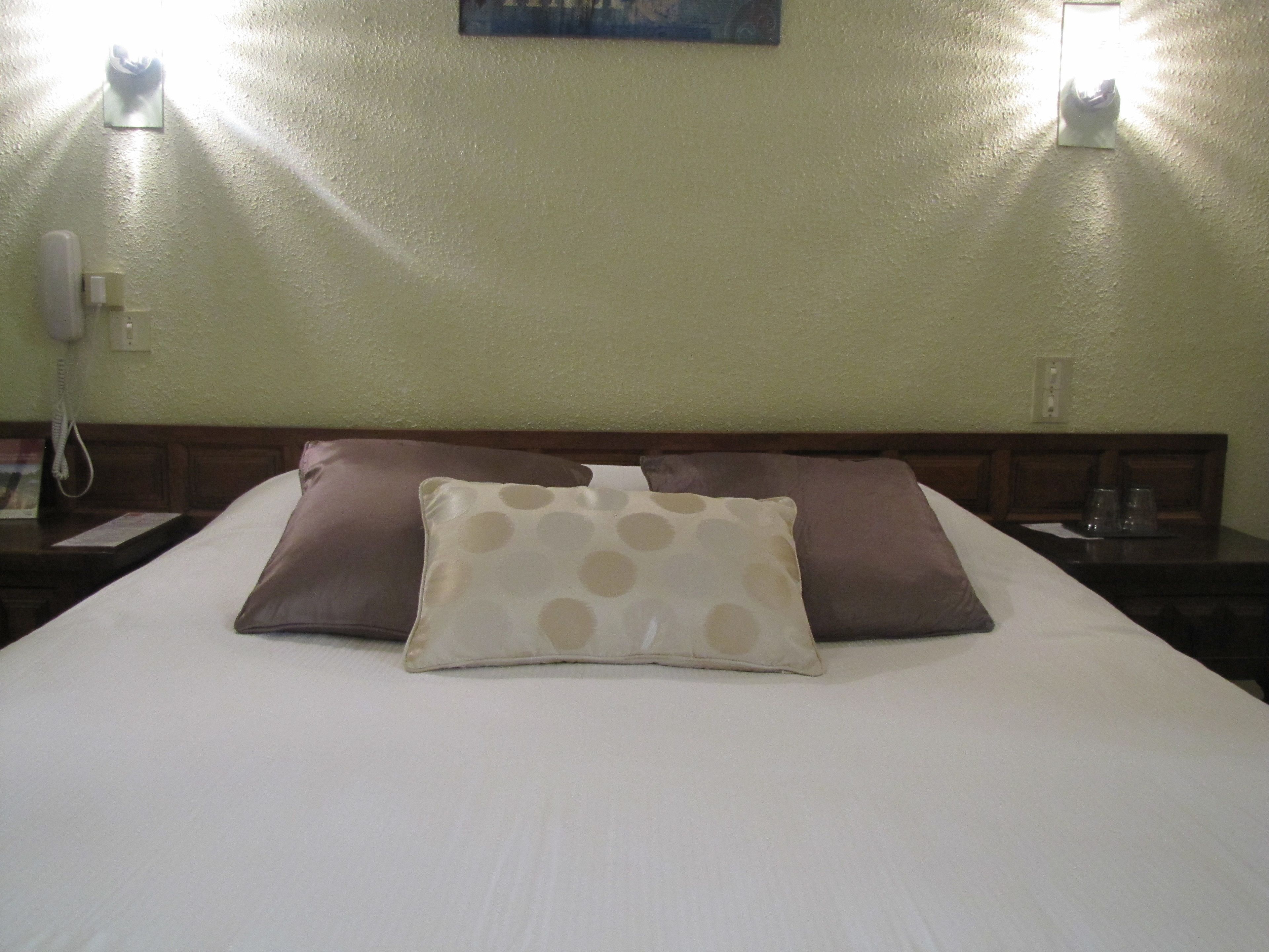 A hotel room with a bed, two pillows, a nightstand, a telephone, and wall sconces.