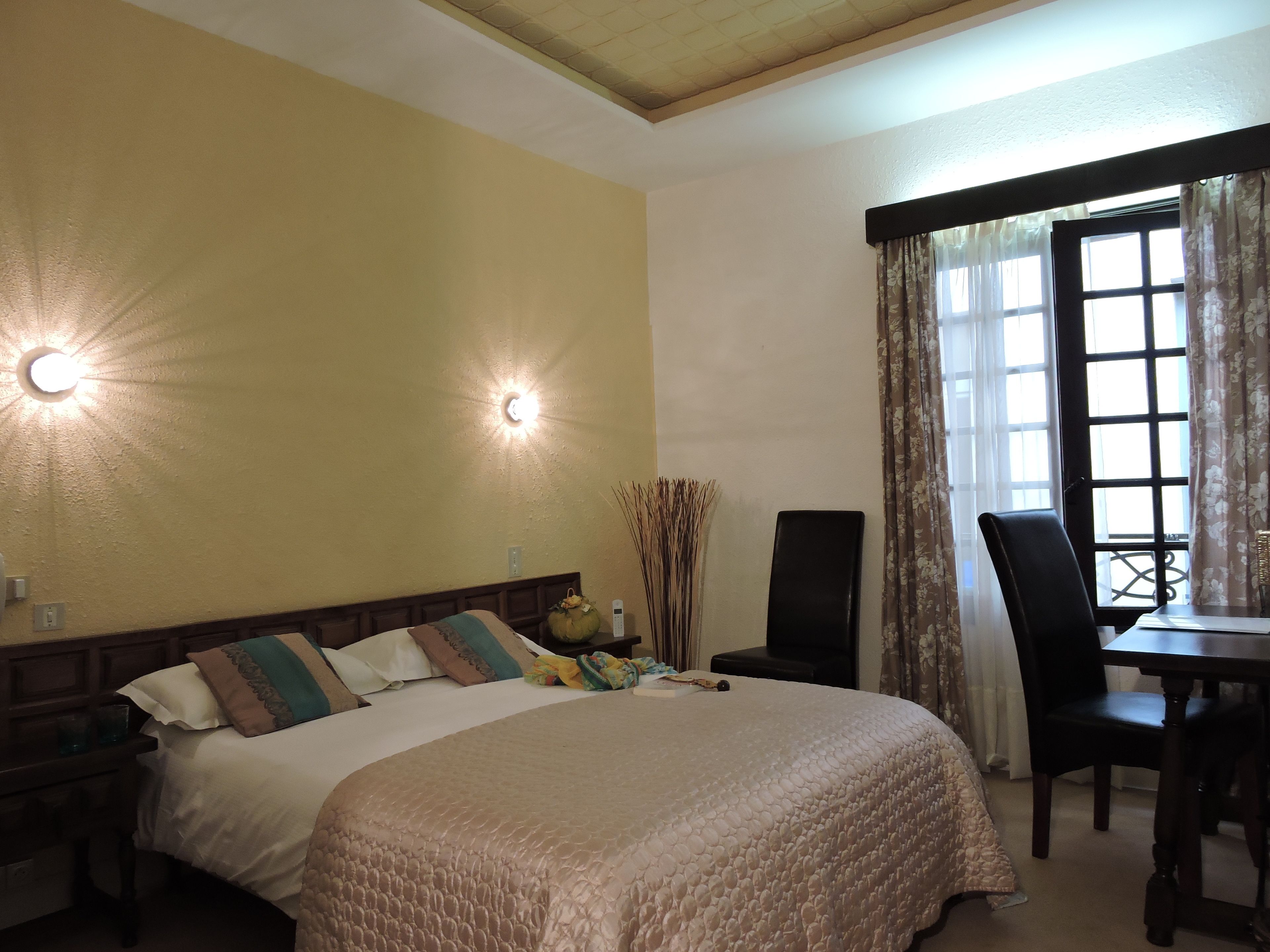 A bedroom with a bed, bedside table, lamp, chair, and a window with curtains.