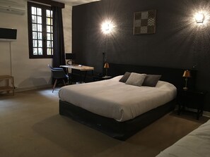 A bedroom with a large bed, a desk, and two bedside lamps. - Hôtel De La Loge (Perpignan)
