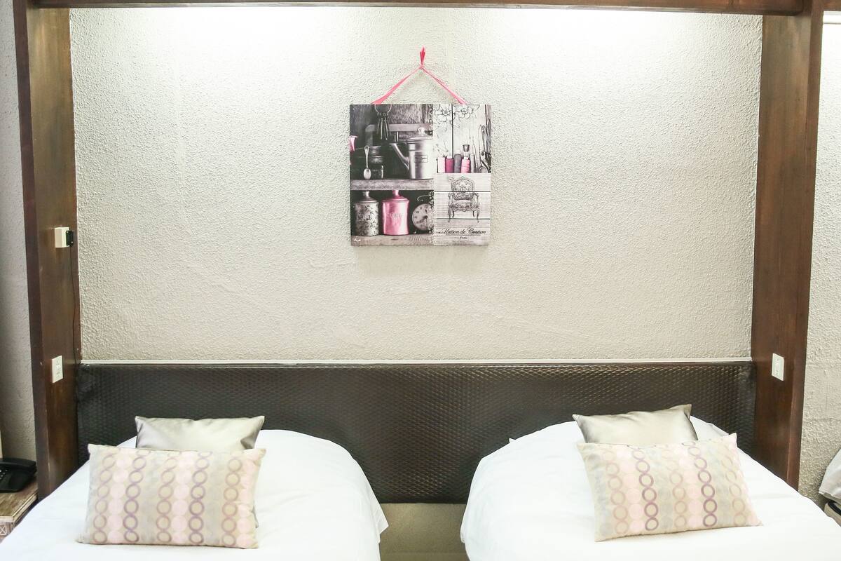Habitación de hotel con dos camas, cabecero de madera y un cuadro colgado en la pared.