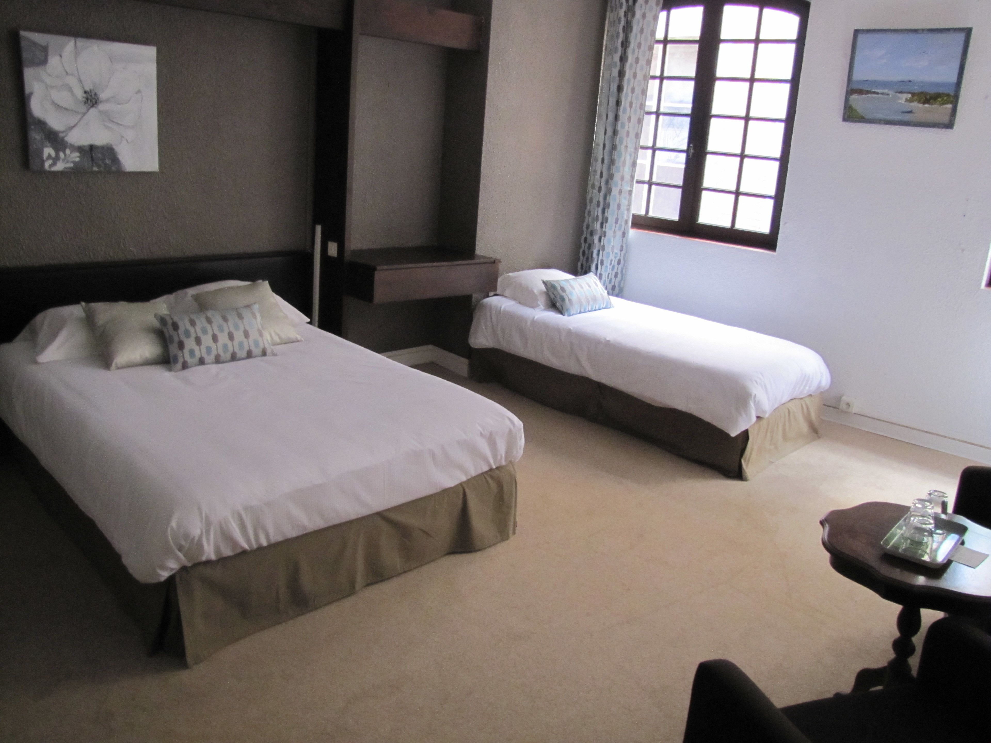 Een hotelkamer met twee bedden, een tafeltje en een raam met gordijnen.